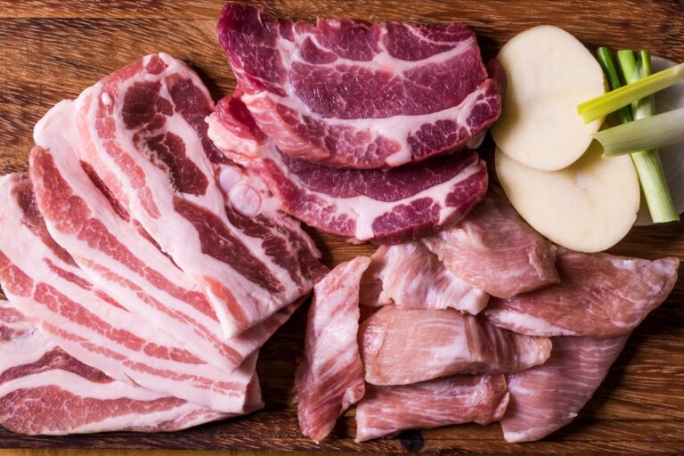 Assorted raw meat cuts displayed on a wooden chopping board with sliced potatoes and spring onions.